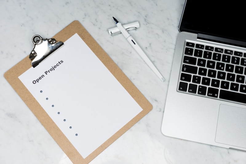 Wooden clipboard with an Open Projects checklist beside a laptop on a marble desk